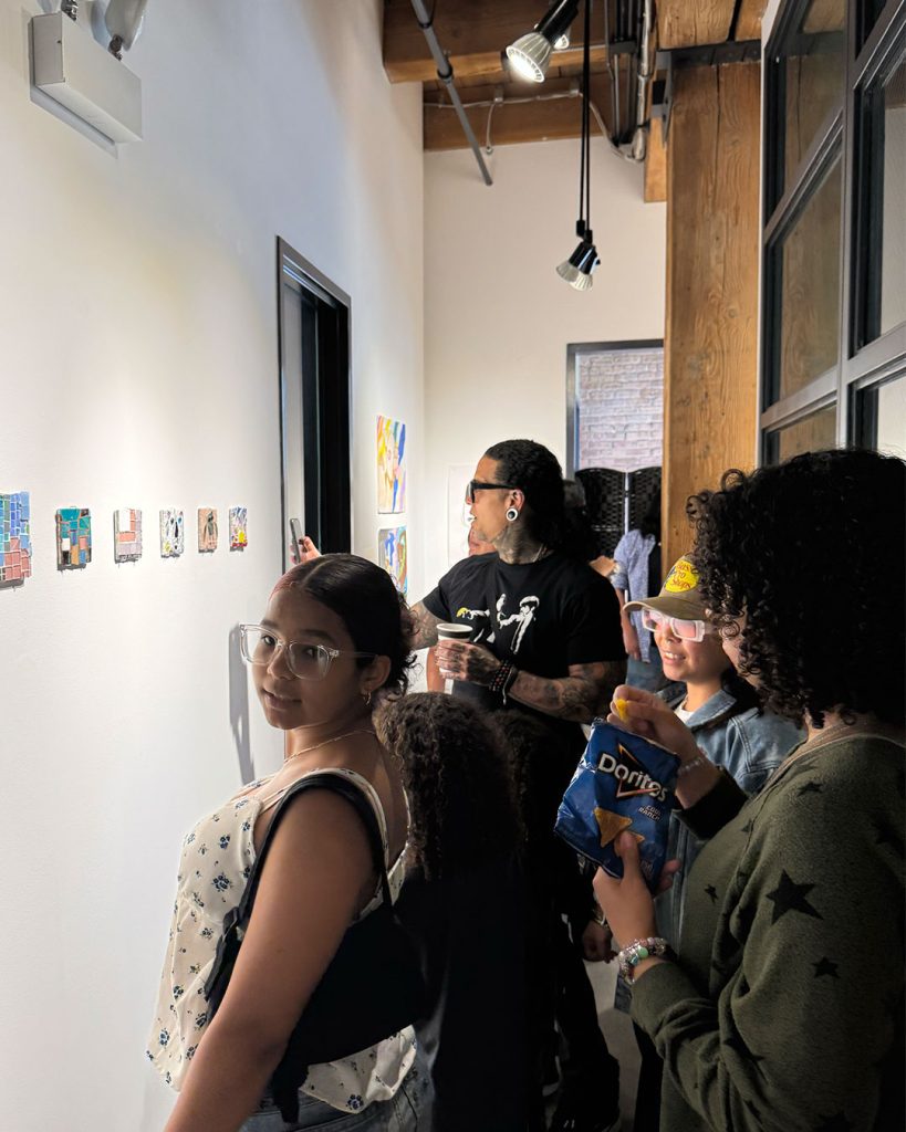 People attending an exhibition at Marwen, looking at paintings mounted on the walls.