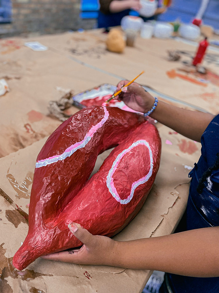 A young artist stylistically paints a large papier mache sculpture of lips.