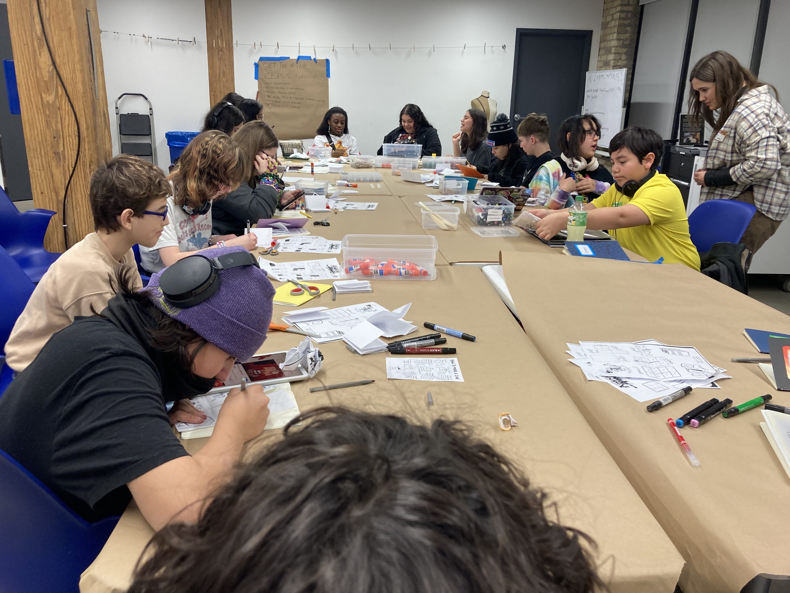 Young artists gather around the table as they create comics and zines.