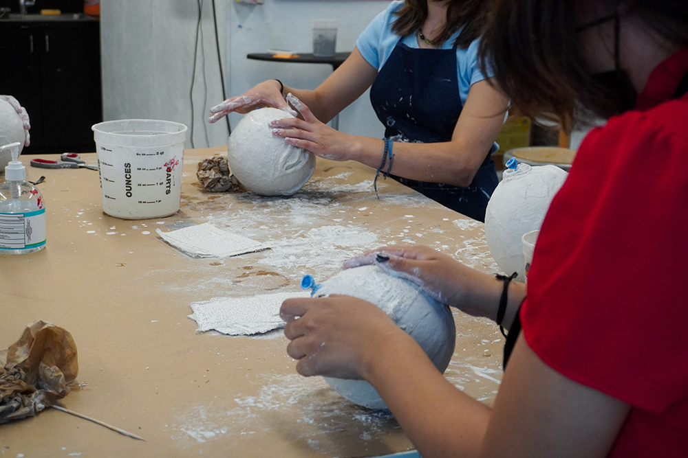 A close up image of hands smoothing papier mache spheres.