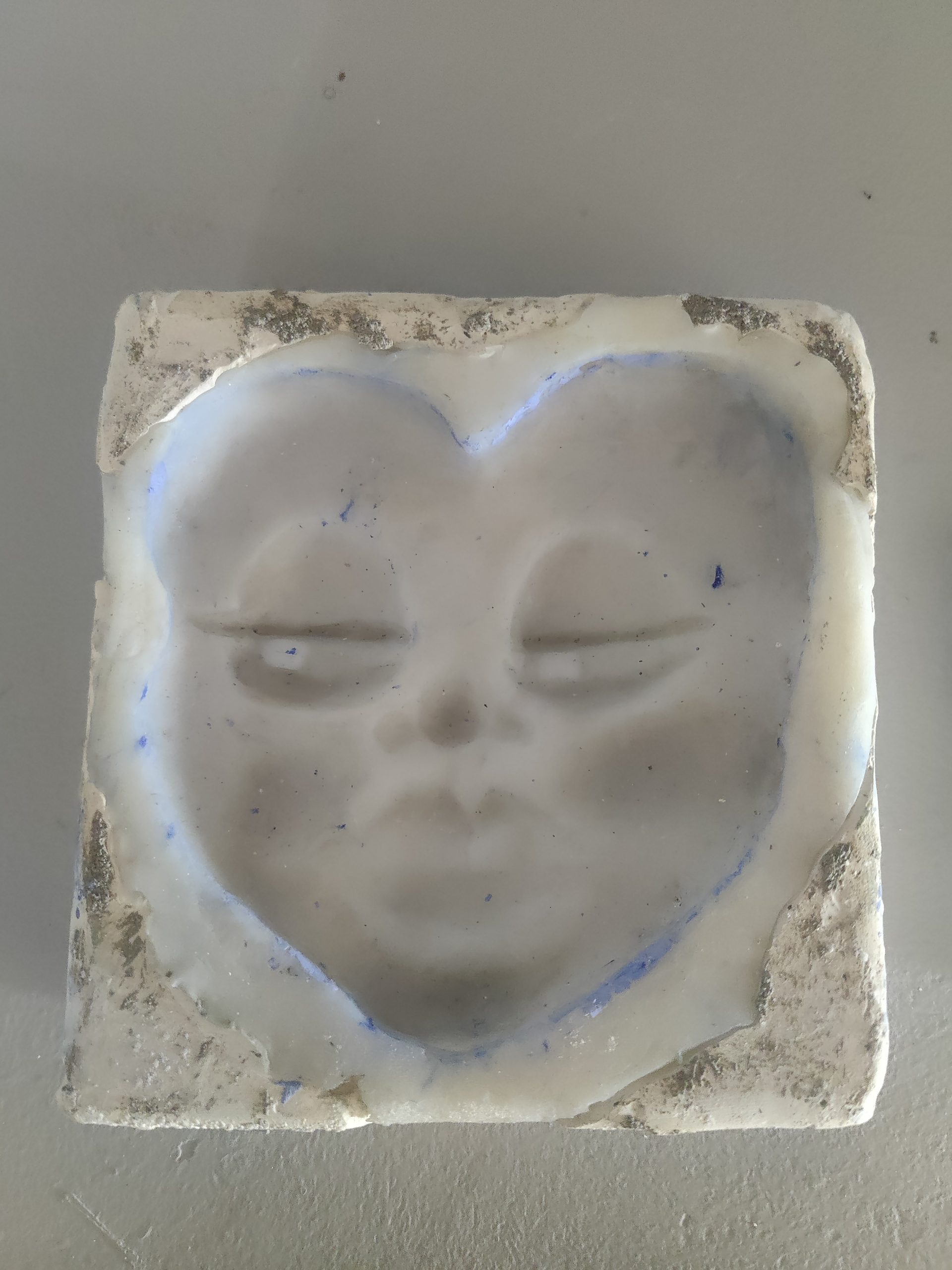 White plaster relief of a sleeping face on a square block with closed eyes and a subtle blue outline edge