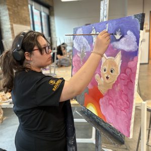 Sp26_MarwenLAB_IMG_4823 - Marwen A young artist works on a colorful painting featuring cats in clouds in Marwen LAB.